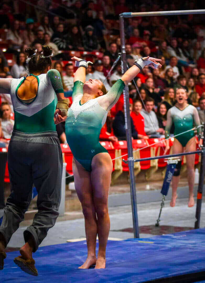 Gymnast celebrating a successful routine on the uneven bars, surrounded by cheering crowd, only at Ceek Next Innovations.